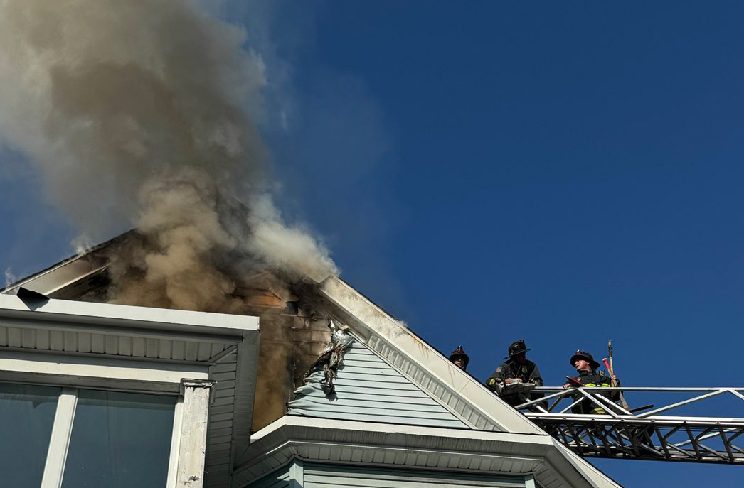 Firefighters on ladder approach fire in attic