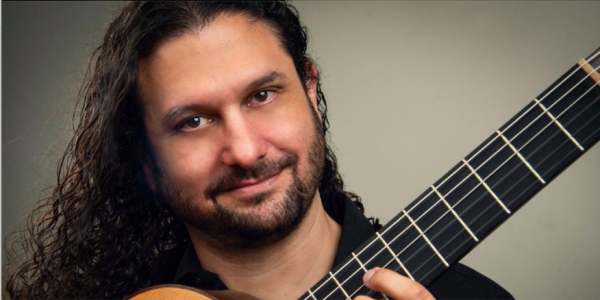 A headshot of guitarist Aaron Largat-Caplan holding a guitar.