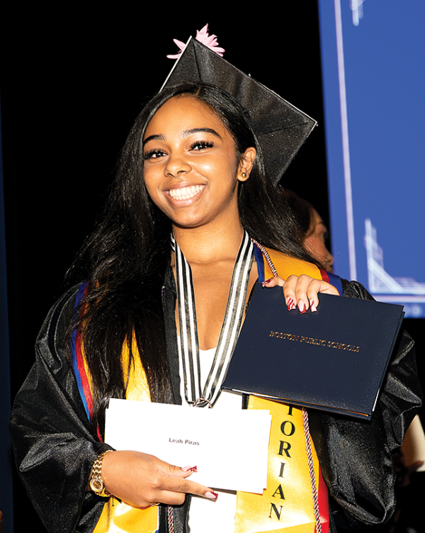 A smiling woman in graduation regalia looks at the camera.